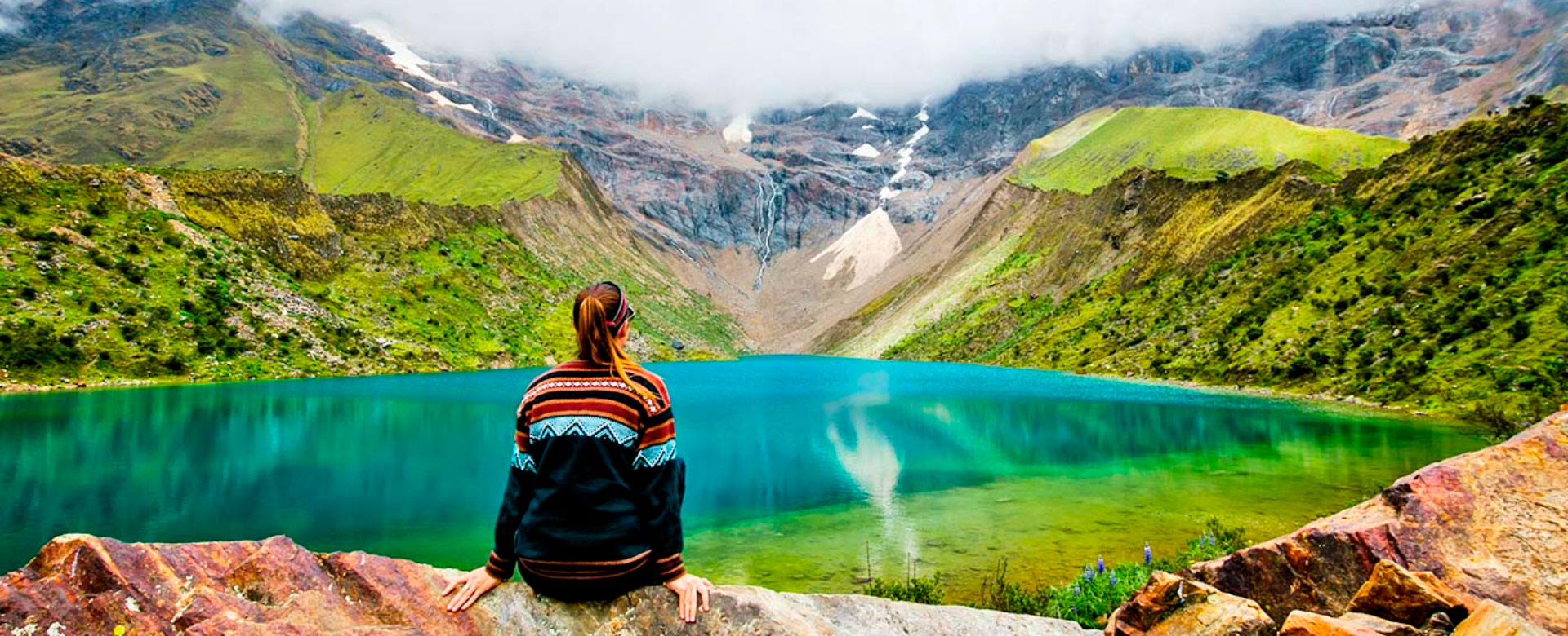 A woman sitting on top of a rock near a lake.