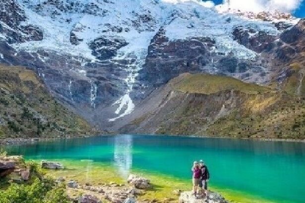 Two people standing on a rock near the water.