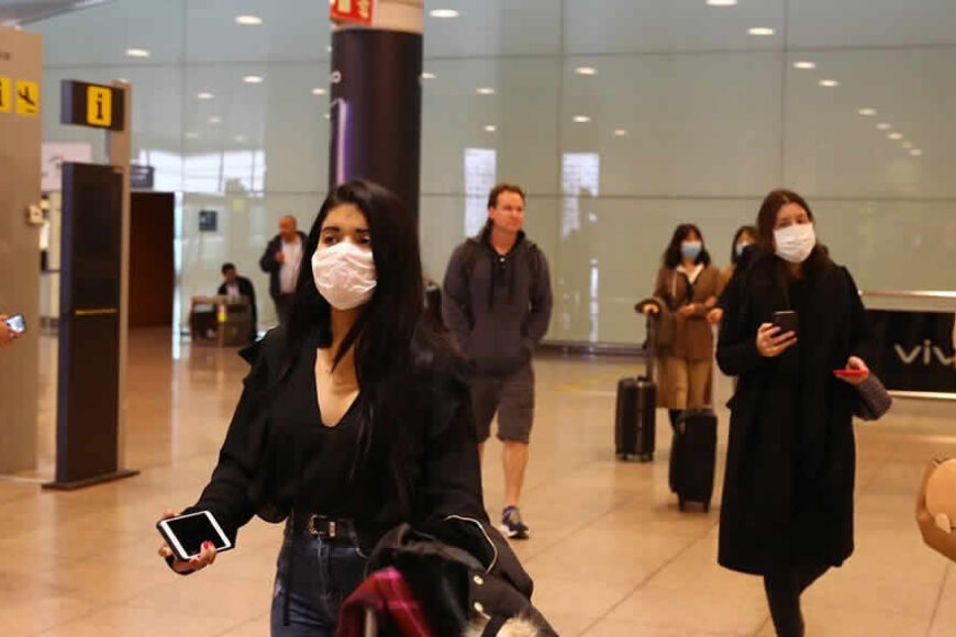 Masked travelers in airport terminal.