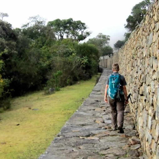 Hiker walks Inca trail stone wall.